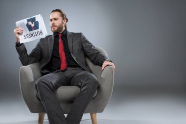 Koltukta oturan ve gri izole gazetede beyaz sakallı işadamı  