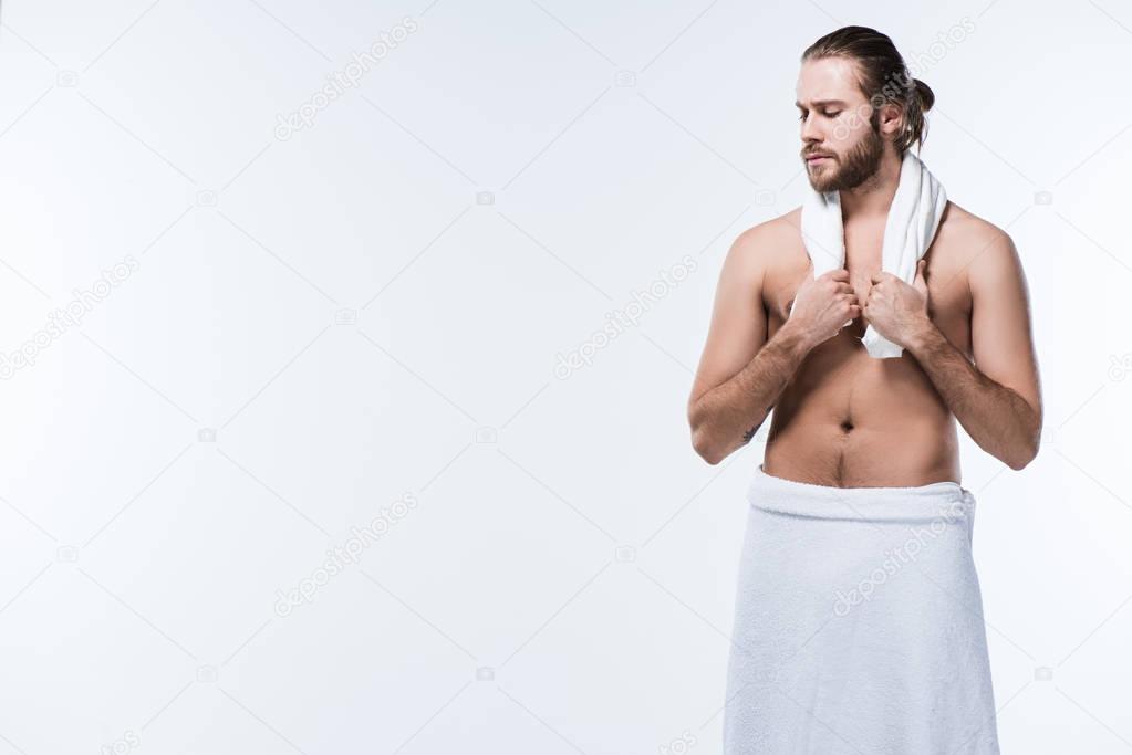 Half naked man with bath towel around his neck and waist, looking down, isolated on white