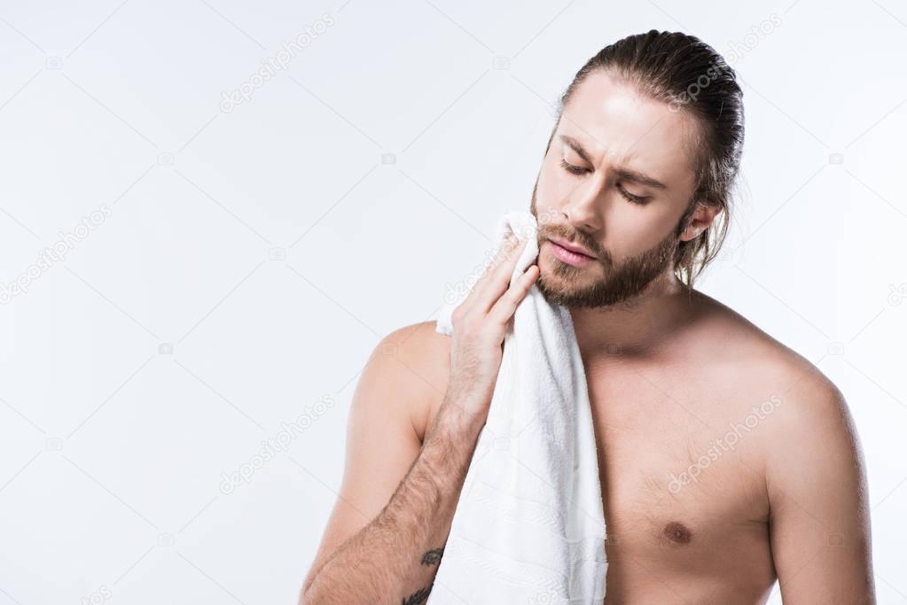 Bearded caucasian man with wet hair holding bath towel in hands while his eyes closed, isolated on white