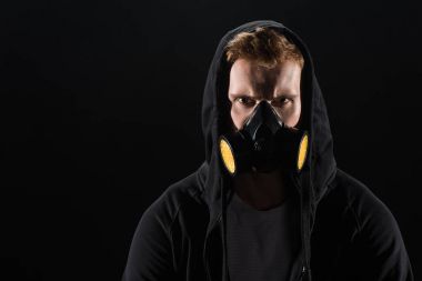 Man in black hood wearing protective filter mask isolated on black clipart