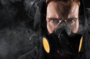 Man in black hood wearing protective filter mask surrounded by clouds of smoke clipart