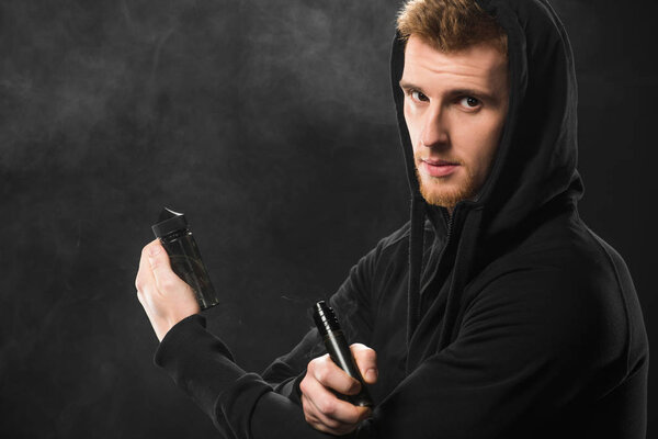 Young bearded man vaping electronic cigarette surrounded by clouds of steam