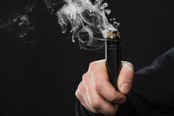 Cropped view of male hand activating electronic cigarette on black background