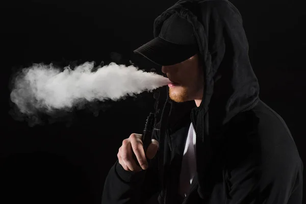 Joven Barbudo Con Gorra Exhalando Humo Cigarrillo Electrónico Aislado Negro — Foto de Stock