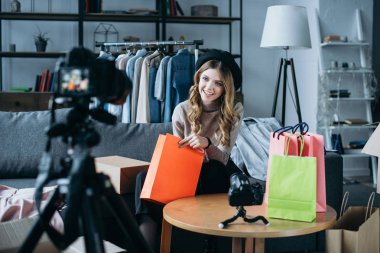 alışveriş torbaları ile oturan ve vlog için yeni video kaydı moda blogger gülümseyen 
