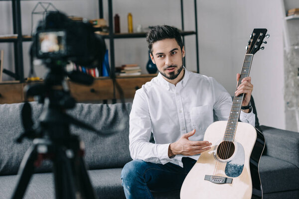 handsome music blogger holding and describing acoustic guitar 