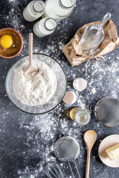 flat lay with flour and other ingredients for bakery, kitchenware on dark tabletop