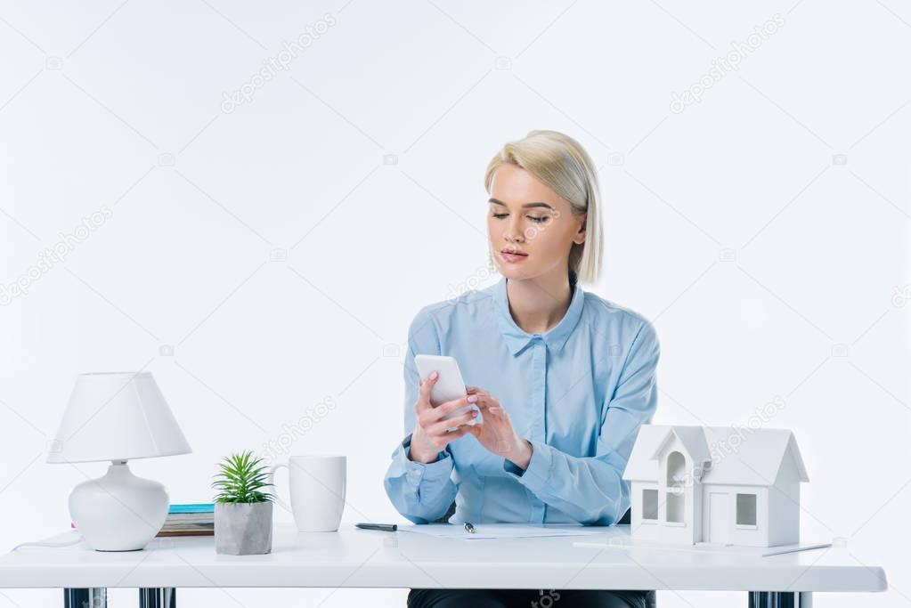 portrait of real estate agent using smartphone at workplace with house model
