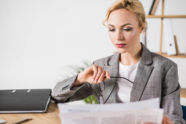 businesswoman with eyeglasses in hand reading newspaper at workplace