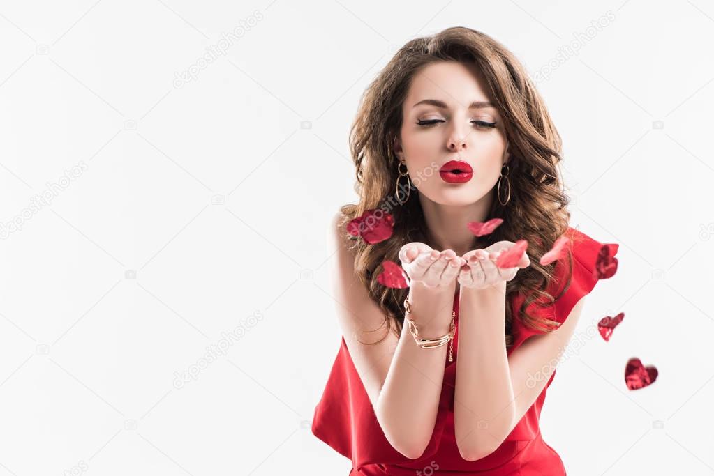 fashionable girl blowing on heart shaped confetti isolated on white, valentines day concept  