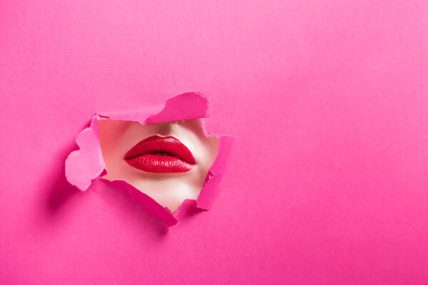 cropped image of passionate girl showing lips in hole in pink paper