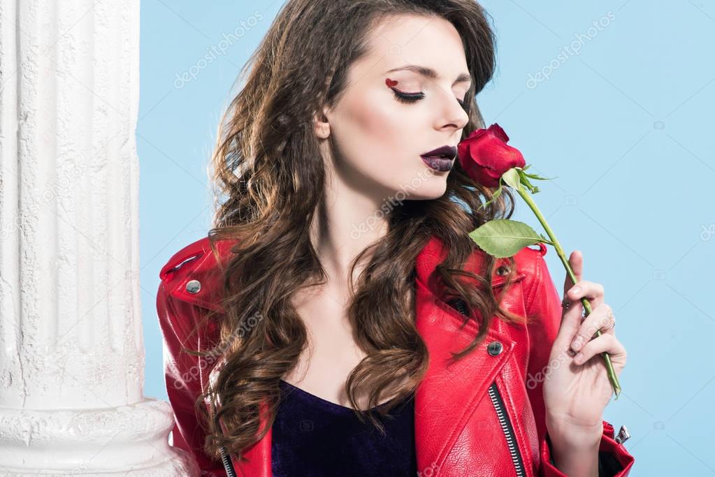attractive girl sniffing red rose isolated on blue, valentines day concept  