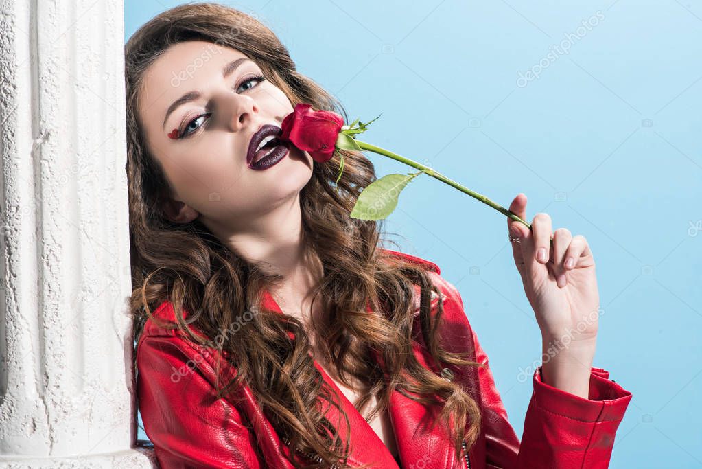 seductive girl touching mouth with red rose isolated on blue, valentines day concept  