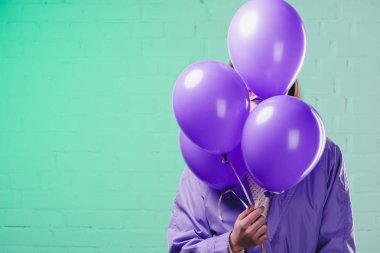 young woman in coat hiding behind purple helium balloons clipart