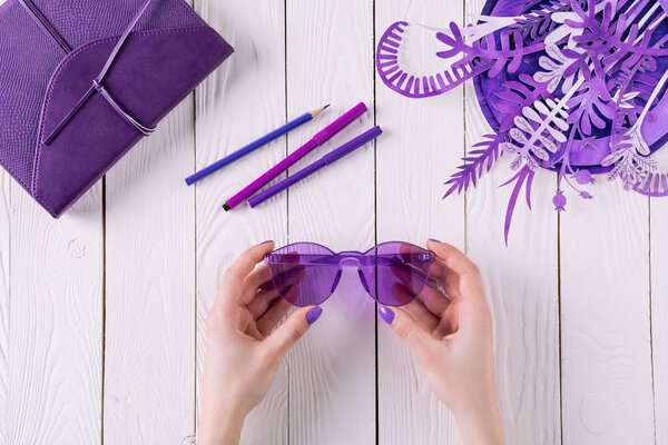 cropped shot of woman holding purple eyeglasses over table