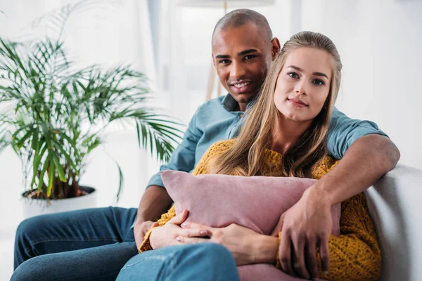 Multicultural Couple Hugging Sofa Looking Camera — Stock Photo, Image