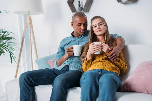 多文化情侣拥抱 坐在沙发上与咖啡 — 图库照片