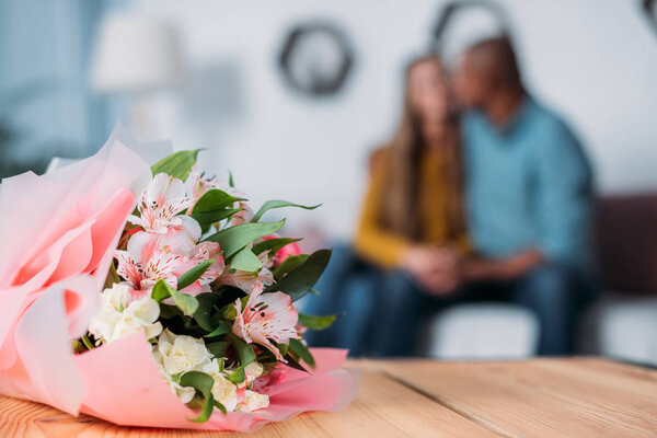 multicultural couple kissing with bouquet on foreground