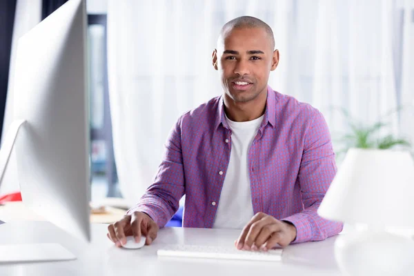 Leende Afroamerikanska Man Sitter Vid Datorn Och Tittar Kameran — Stockfoto