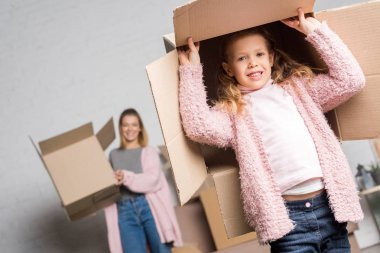 happy mother and daughter holding cardboard boxes while moving home clipart