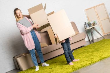 happy mother and little daughter holding cardboard boxes while moving home clipart