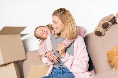 happy mother and daughter hugging while sitting on sofa during relocation clipart