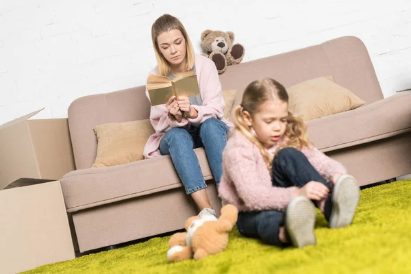 Kid Playing Teddy Bear Carpet While Mother Reading Book Sofa — Stock Photo, Image