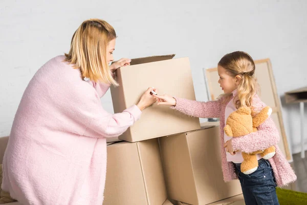 Mother Daughter Teddy Bear Signing Cardboard Boxes While Relocating — Stock Photo, Image