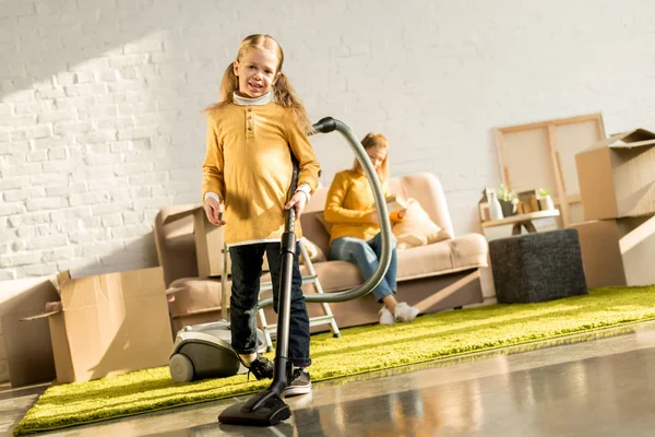 Sorrindo Criança Pequena Sala Limpeza Com Aspirador Enquanto Mãe Ler — Fotografia de Stock