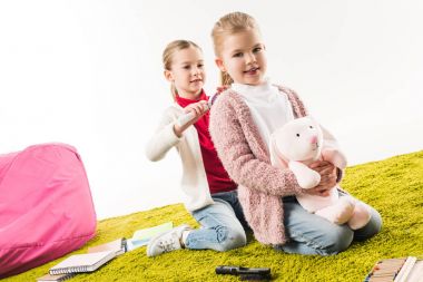 one sister brushing hair of another while she sitting on floor with toy bunny isolated on white clipart