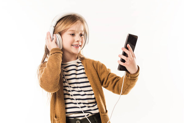 happy little child listening music with headphones and taking selfie isolated on white