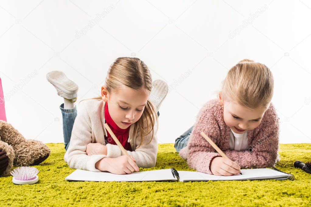 focused little sisters drawing with color pencils together on floor isolated on white