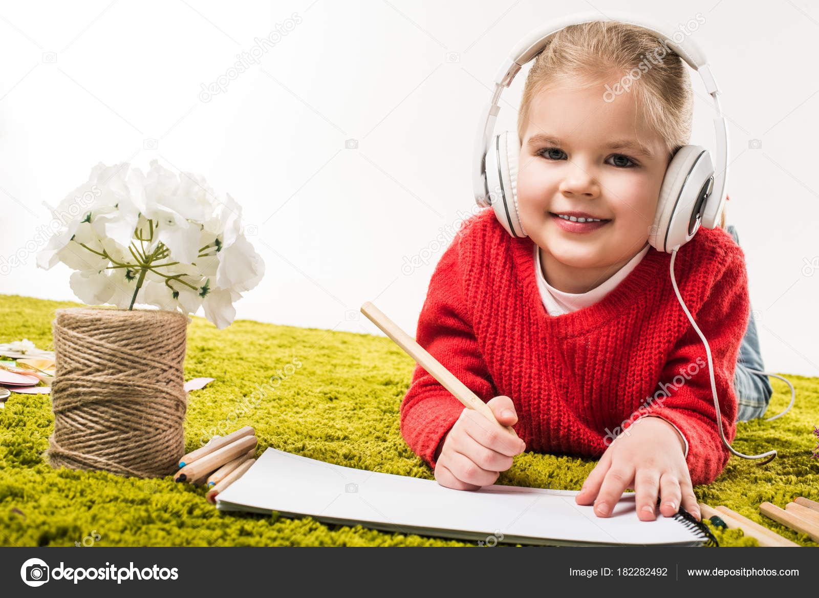 Piccolo bambino felice disegno con matite di colore e l ascolto di musica sul tappeto morbido verde isolato su bianco — Foto di EdZbarzhyvetsky