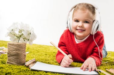 renkli kalemler ile çizim ve yeşil yumuşak halı üzerinde beyaz izole müzik dinlerken mutlu küçük çocuk