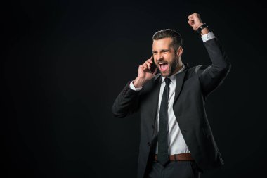 excited businessman in jacket celebrating while talking on smartphone, isolated on black clipart