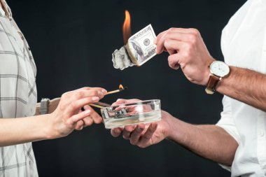 cropped view of businesspeople burning dollar banknotes, isolated on black clipart