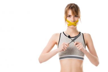 young woman with measuring tape tied around her mouth holding fork and knife isolated on white clipart
