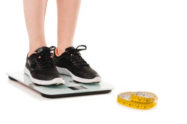 cropped shot of woman standing on scales with measuring tape lying on floor isolated on white clipart