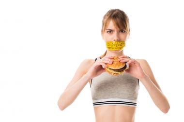 Teyp üzerinde beyaz izole burger tutan ölçme genç ince kadın ağzını ile bağlı
