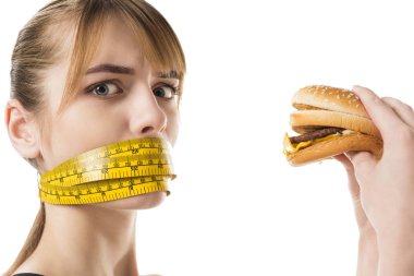 young woman with mouth tied in measuring tape trying to eat burger isolated on white clipart