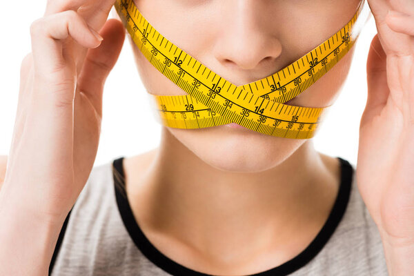 cropped shot of woman with measuring tape tied around her mouth touching head isolated on white