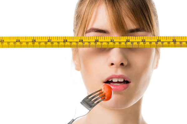 young woman eating cherry tomato with measuring tape in front her eyes isolated on white