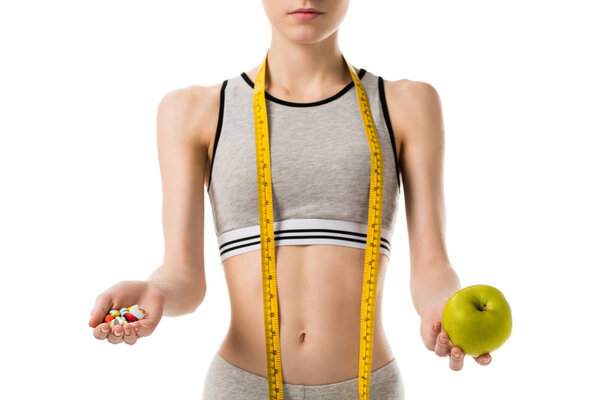 cropped shot of young slim woman holding fresh apple and pills isolated on white