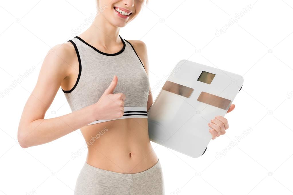 cropped shot of happy slim woman holding scales and showing thumb up isolated on white