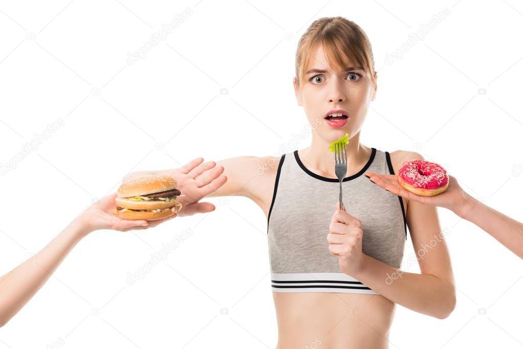young slim woman refusing of junk food and eating broccoli isolated on white
