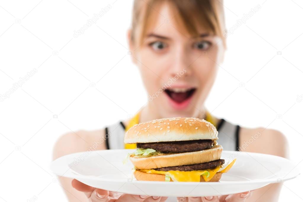 excited young woman looking at burger on plate isolated on white