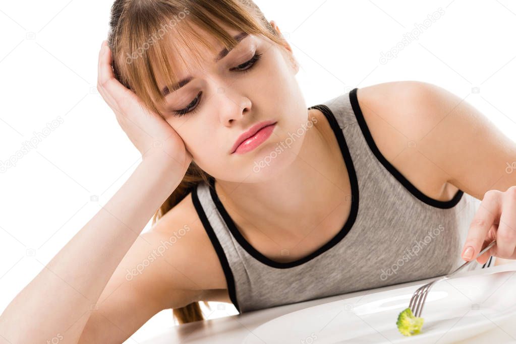 sad slim woman eating piece of broccoli from plate isolated on white