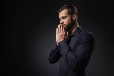 side view of man praying isolated on black
