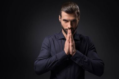 portrait of man looking at camera while praying isolated on black clipart