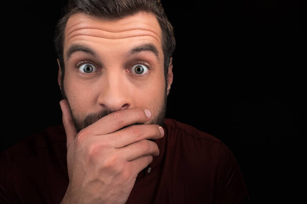 portrait of shocked man covering mouth isolated on black